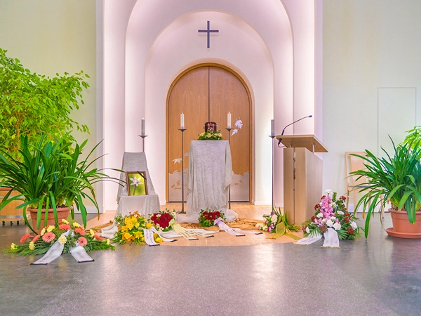 Eine festlich dekorierte Urne steht im Mittelpunkt eines Trauerschwals, umgeben von Blumenarrangements, Kerzen und einem Rednerpult. Die Szene vermittelt eine Atmosphäre der Ruhe und des Abschieds. Bestattungsfotografie von Michael Schalansky.