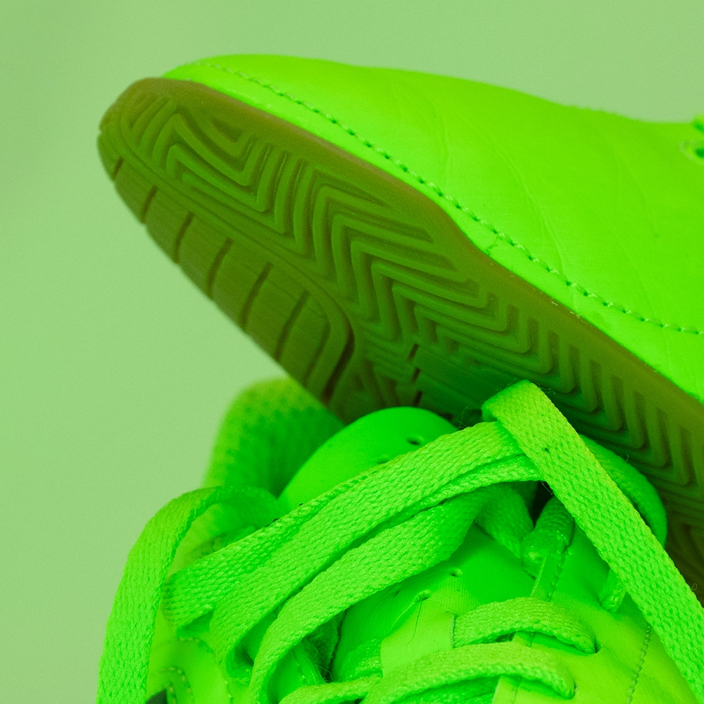 Detail eines neonfarbenen Fußballschuhs unter grünem LED-Licht mit geringerer farblicher Trennung zwischen Materialien.