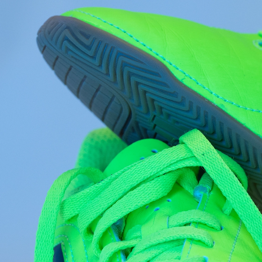 Detail von Sohle, Naht und Schnürsenkeln eines neonfarbenen Fußballschuhs unter kühlem LED-Licht.