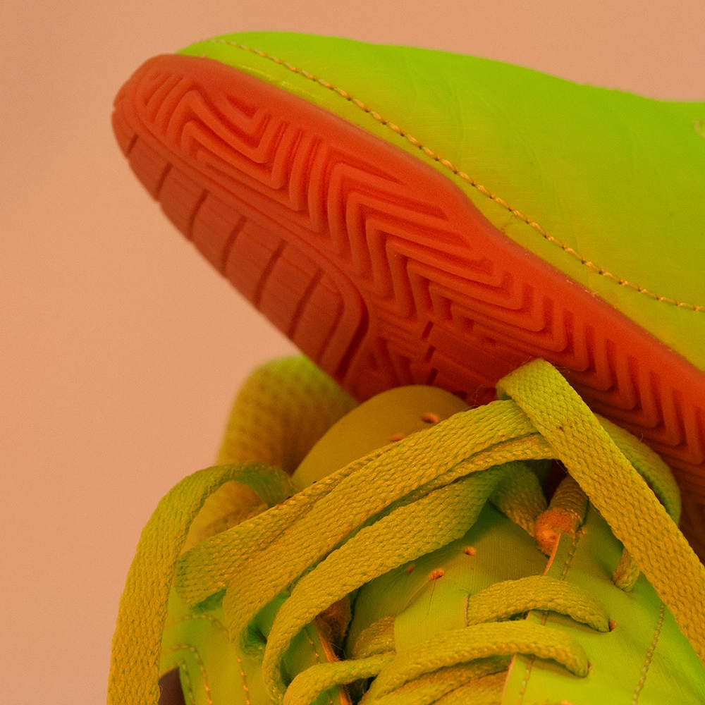 Detail eines neonfarbenen Fußballschuhs unter warmem orangefarbenem LED-Licht mit veränderter Material- und Sohlenfarbe.