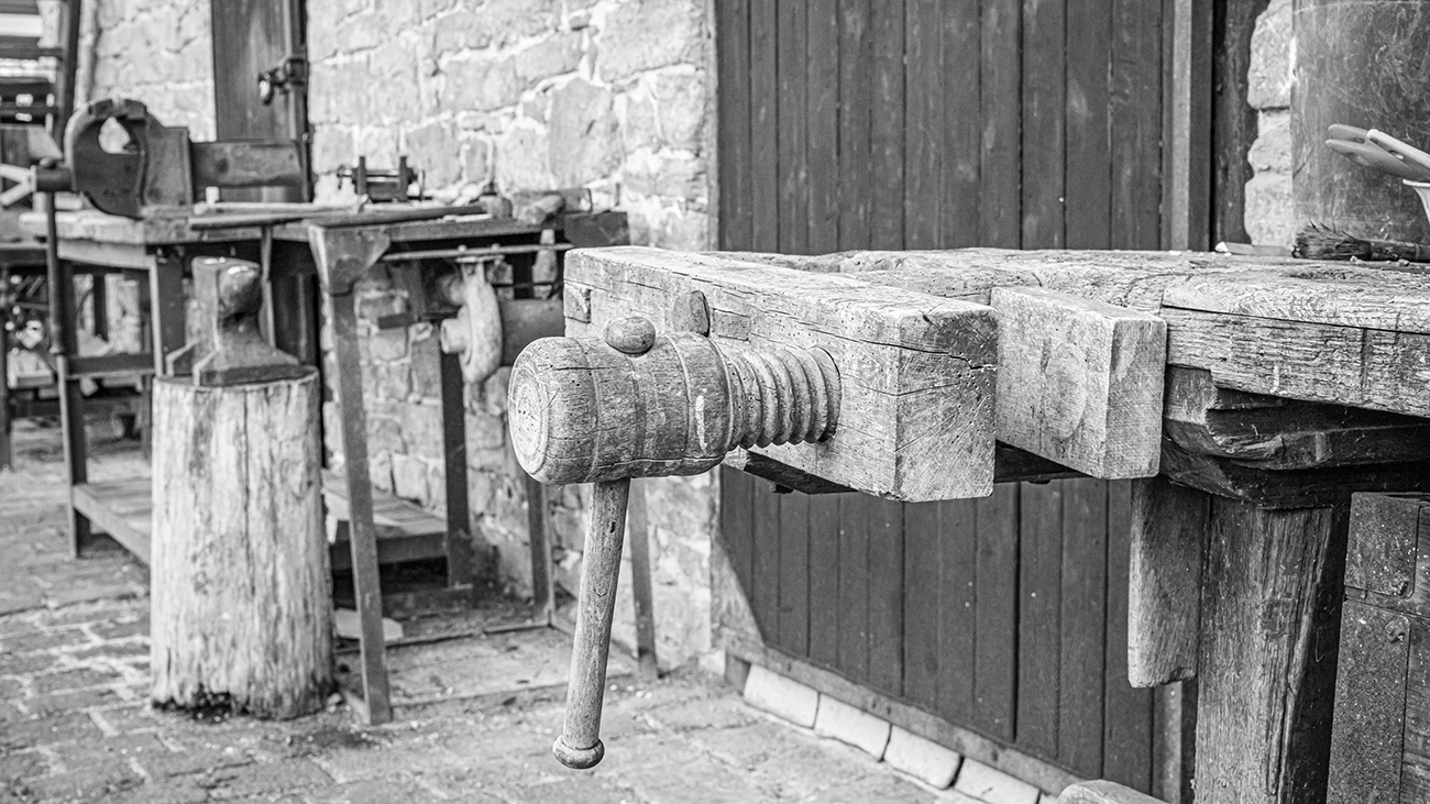 Schwarz-Weiß-Foto einer Werkbank mit Schraubstock und deutlich erkennbaren Details im Vorder- und Hintergrund als Beispiel für größere Schärfentiefe.