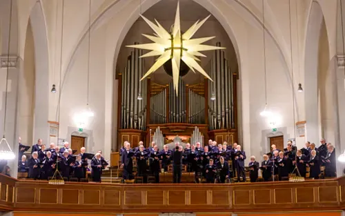 Erfurter Männerchor auf der Empore einer Kirche während eines Konzerts mit Dirigent und Orgel im Hintergrund.