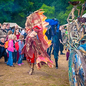 Darstellerin im aufwendigen Feuervogel-Kostüm mit ausgebreiteten orange-roten Flügeln beim Mittelalterfest MPS Bückeburg vor Publikum.