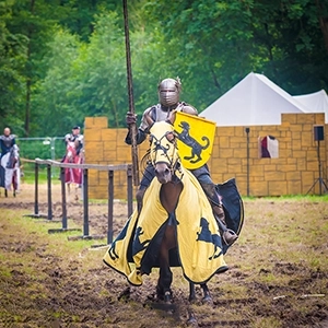 Ritter in voller Rüstung reitet mit Lanze und gelbem Wappenschild auf einem geschmückten Pferd beim Mittelalterfest MPS Bückeburg.