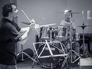 Schwarz-Weiß-Aufnahme eines Schlagzeuglehrers, der einem Schüler am Drumset Anweisungen gibt – konzentrierter Unterrichtsmoment in Erfurt.