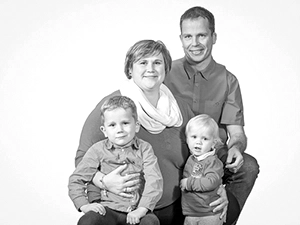 Schwarz-weißes Familienporträt von einer lächelnden vierköpfigen Familie – Eltern mit zwei kleinen Kindern – im Fotostudio vor weißem Hintergrund. Ein klassisches und zeitloses Familienbild, professionell erstellt von Michael Schalansky Fotografie in Erfurt.