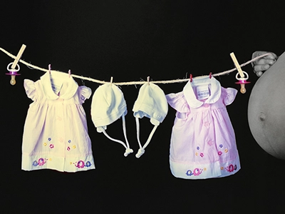 Babybauch-Fotoshooting mit aufgehängter Babykleidung vor dunklem Hintergrund – Schwangerschaftsfotografie in Erfurt.