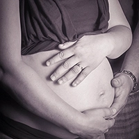 Detailaufnahme eines schwangeren Bauches in Sepiatonung, umarmt von den Händen der werdenden Mutter und des Partners. Ein Ring an ihrem Finger ist sichtbar. Dieses Bild symbolisiert Liebe und Vorfreude, professionell festgehalten von Fotograf Michael Schalansky.