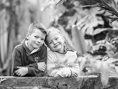 Geschwisterporträt im Palmenhaus Erfurt – zwei Kinder lehnen lächelnd an einer Steinmauer, Schwarz-Weiß-Aufnahme in natürlicher Umgebung.