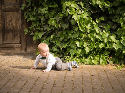 Kleines Kind krabbelt auf Pflasterweg vor Holztür und Efeu – natürlicher Moment in Erfurt, festgehalten als Kinderfotografie.