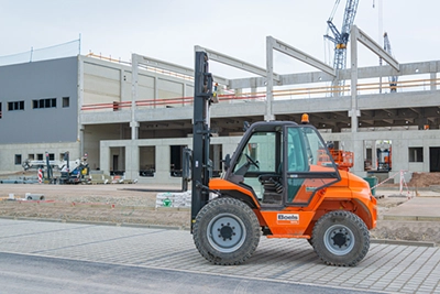 Boels Teleskoplader auf Baustelle vor Gebäude im Bau, Maschinen und Kräne im Hintergrund.