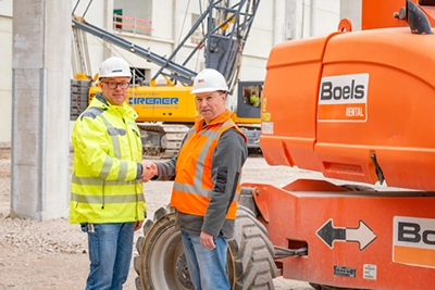 Businessporträt auf der Baustelle: Zwei Personen geben sich die Hand vor einem Boels Gerät – Firmenfotografie von Michael Schalansky.