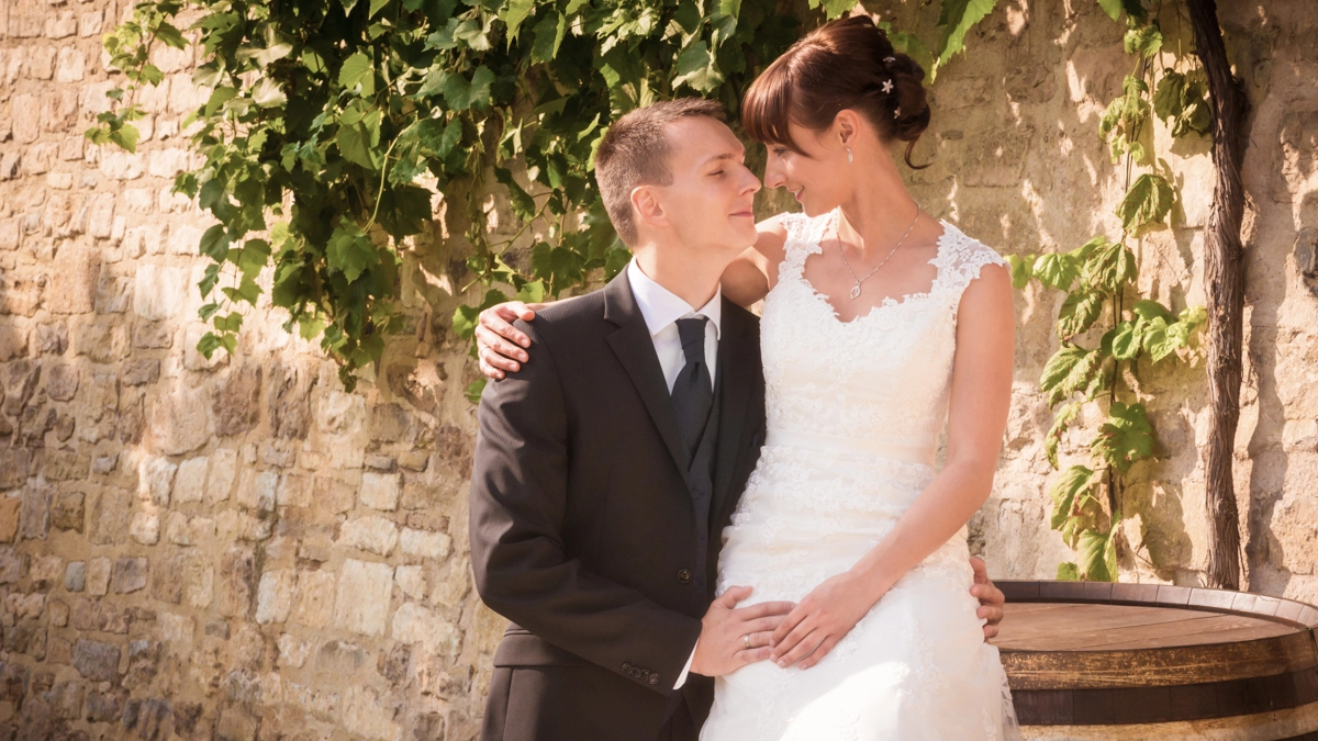 Brautpaar_Petersberg_Erfurt_Hochzeit_Romantik_Michael-Schalansky Romantisches Hochzeitsfoto eines Brautpaares am Petersberg in Erfurt. Sie stehen eng umschlungen vor einer historischen Steinmauer mit Efeu. Der Bräutigam blickt liebevoll zur lächelnden Braut. Ein Beispiel für authentische und emotionale Hochzeitsfotografie in historischen Kulissen von Michael Schalansky.