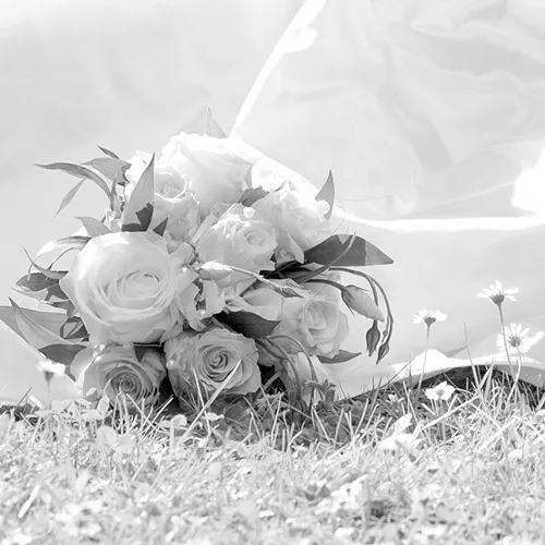 Schwarz-Weiß-Hochzeitsdetail: Brautstrauß liegt im Gras, Schleierstoff im Hintergrund – Hochzeitsfotografie von Michael Schalansky in Erfurt und Thüringen.
