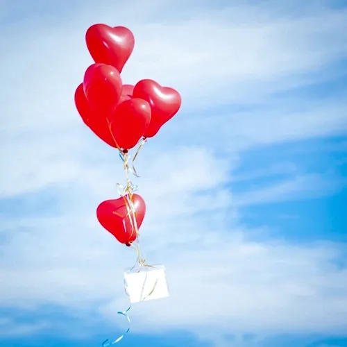 Hochzeitsdetail: rote Herzluftballons steigen in den Himmel, eine kleine Karte hängt an den Bändern – Symbolfoto Hochzeit von Michael Schalansky in Erfurt und Thüringen.