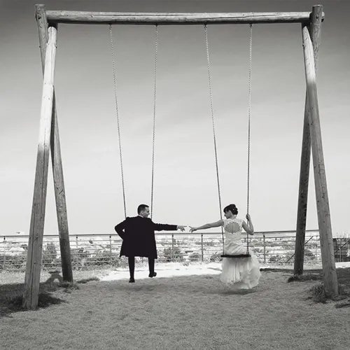 Schwarz-Weiß-Hochzeitsfoto in Thüringen: Brautpaar auf einer riesigen Holzschaukel, Hand in Hand – kreatives Paarshooting von Michael Schalansky.