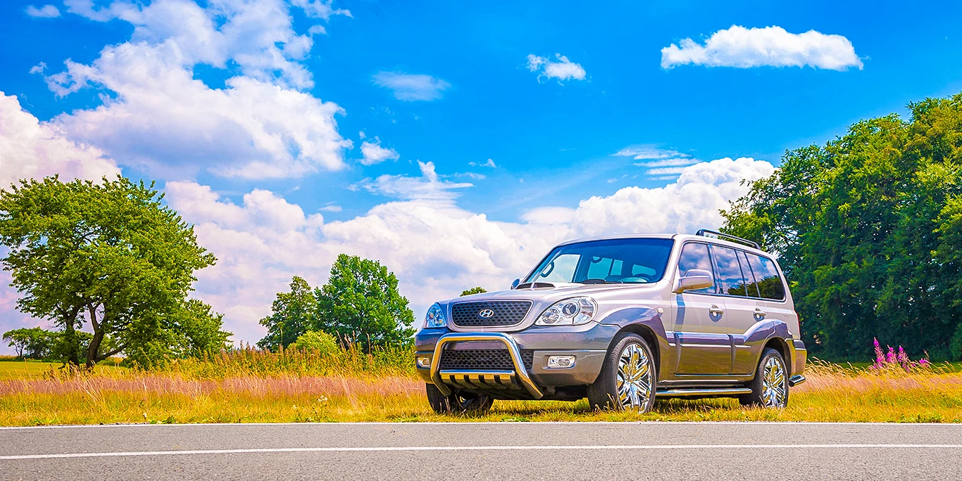 Silberner Hyundai-Geländewagen als On-Location-Produktfotografie am Straßenrand vor sommerlicher Landschaft mit blauem Himmel und Wolken.