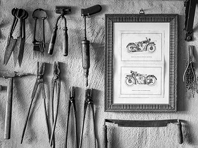 Streetfotografie: Eine Wand mit einer Ansammlung von gebrauchten Handwerkzeugen, die an vergangene Zeiten und handwerkliches Können erinnern, ergänzt durch historische Motorradzeichnungen, eine Hommage an das industrielle Erbe, Schwarz-Weiß von Michael Schalansky.