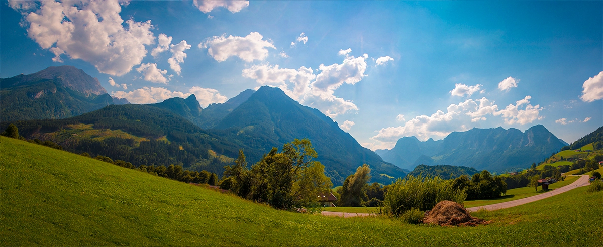 Eine weite, offene Berglandschaft mit grünen Tälern, bewaldeten Hügeln und majestätischen Gipfeln unter einem dynamischen Wolkenhimmel, die ein Gefühl von Freiheit und Abenteuer vermittelt. Fotografie von Michael Schalansky.