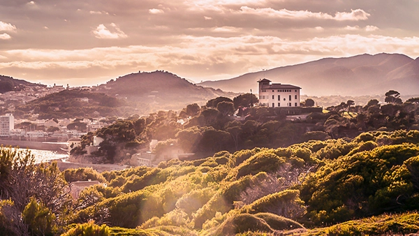 Weitläufige Landschaft mit einem markanten Haus auf einem Hügel, gebadet im warmen, goldenen Licht der späten Sonne, die eine stimmungsvolle und atmosphärische Szene schafft, Fotografie von Michael Schalansky.