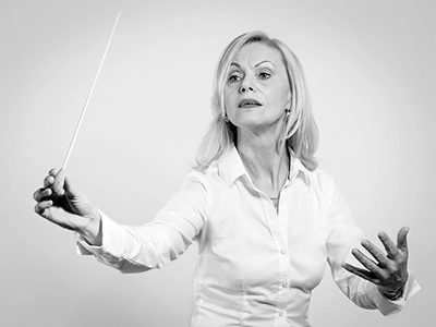 Ausdrucksstarkes Schwarz-Weiß-Porträt einer Dirigentin mit erhobenem Taktstock und fokussiertem Blick.