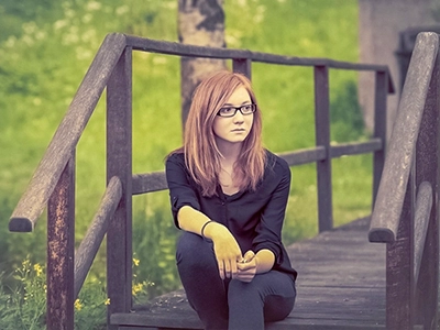 Outdoor-Porträt einer jungen Frau mit Brille auf einer Holzbrücke im Grünen.