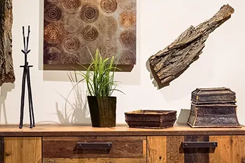 Stilvolle Interieur-Fotografie: Holzkommode mit Deko. Perfekte Inszenierung für Möbelmarken und Einrichtungshäuser. Rustikale Holzkommode mit Dekoration: Pflanzen, Metallskulptur und Wandbilder. Authentische Interieur-Fotografie für Möbel und Wohnaccessoires.