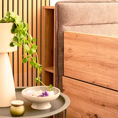 Detailaufnahme eines modernen Familienbettes mit Holzelementen und Stoffbezug, daneben Beistelltisch mit Dekoration und Pflanzen.