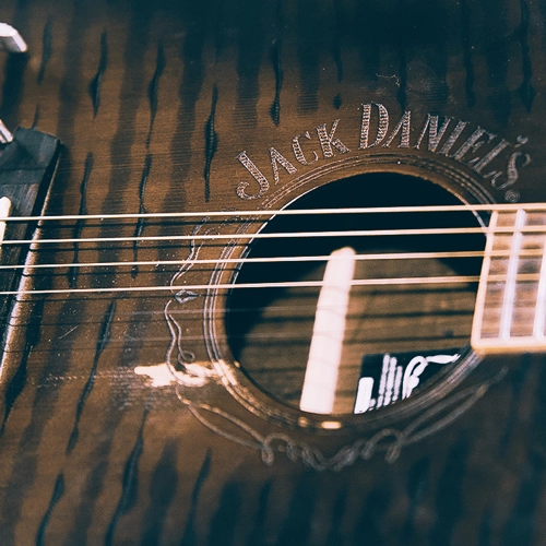 Marken-Inszenierung: Jack Daniel's Gitarre. Ausdrucksstarke Produktfotografie für Lifestyle- und Merchandising-Artikel. Detailansicht einer akustischen Gitarre mit dem eingravierten Jack Daniel's Logo um das Schallloch. Authentische Lifestyle-Produktfotografie.