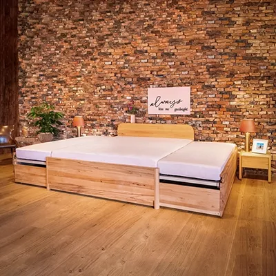 Breites, ausziehbares Familienbett aus Holz in einem wohnlichen Ambiente mit Ziegelwand im Hintergrund.