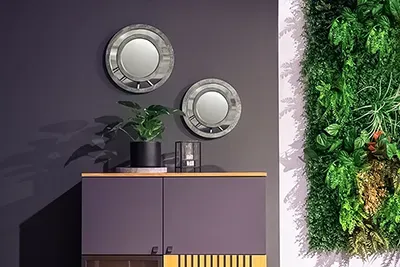 Moderne Wohnzimmer-Inszenierung: Sideboard vor dunkler Wand mit zwei runden Spiegeln und Pflanze, daneben eine vertikale grüne Pflanzenwand.