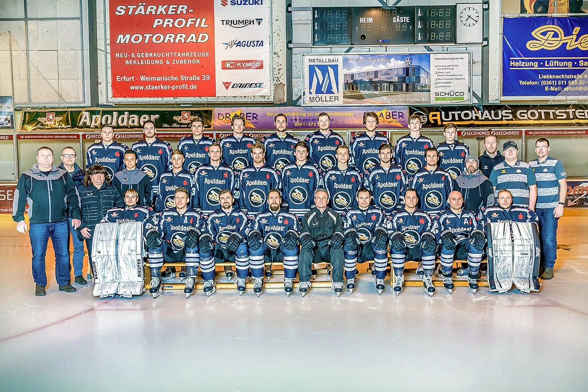 Ein großes Gruppenfoto der Eishockeymannschaft der Black Dragons Erfurt, mit Spielern in Uniform sitzend und stehend, umgeben von Trainern und Staff-Mitgliedern. Im Hintergrund sind Werbebanner von "Apoldaer", "Sparkasse" und "Autohaus Gottstedt" zu sehen.