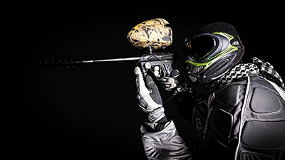 Nahaufnahme eines Paintballspielers mit Maske und Markierer, fokussiert auf das Ziel, isoliert auf dunklem Hintergrund.